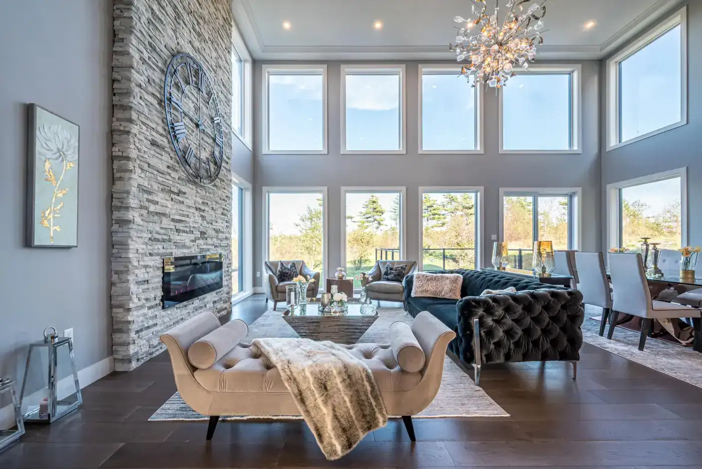 Double-height Halifax living room with a stacked-stone fireplace, full-height windows, and layered seating, designed by MAD Design Interiors